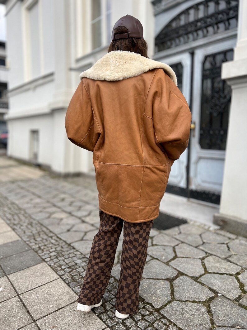 May include: A brown leather jacket with a white shearling collar and brown checkered pants.