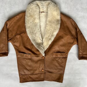 May include: A brown leather jacket with a large white faux fur collar. The jacket has a button closure and two pockets.