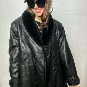 May include: A black leather coat with a faux fur collar and double-breasted closure. The coat has a long length and a relaxed fit.