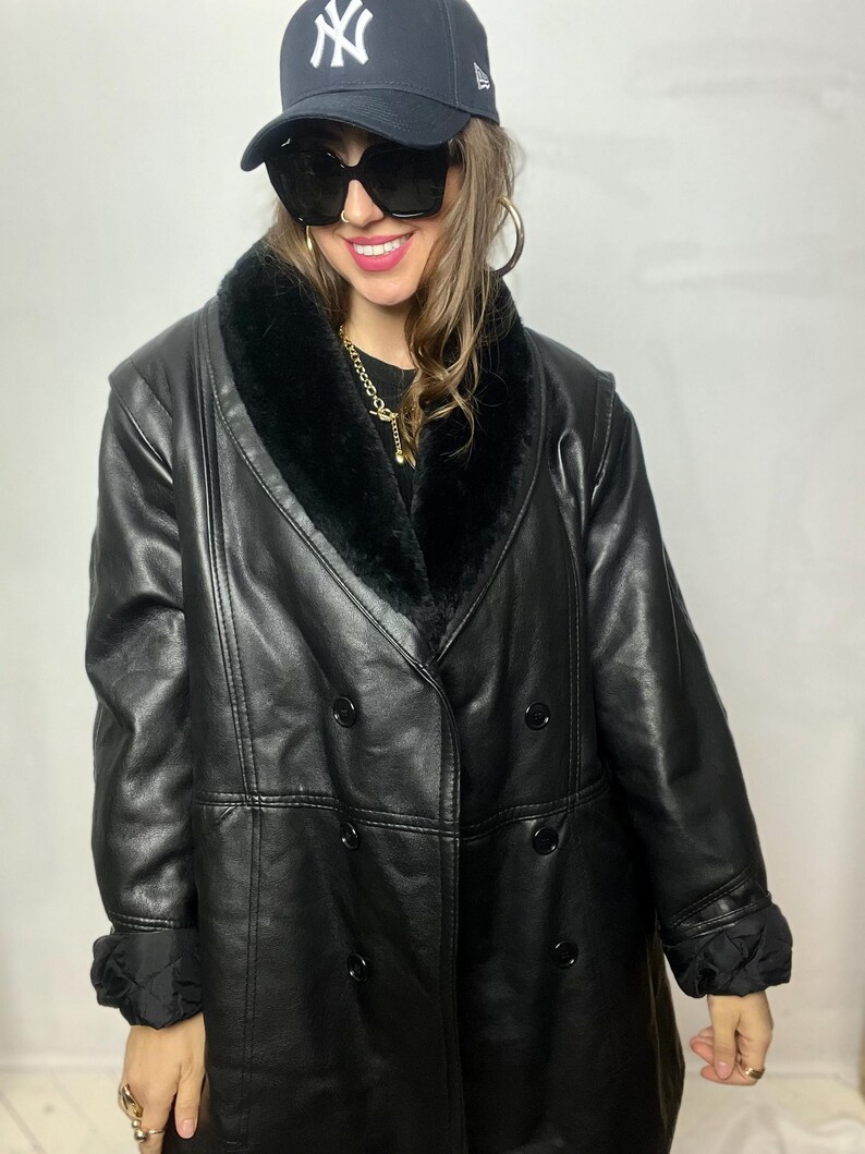 May include: A black leather coat with a faux fur collar and double-breasted closure. The coat has a long length and a relaxed fit.