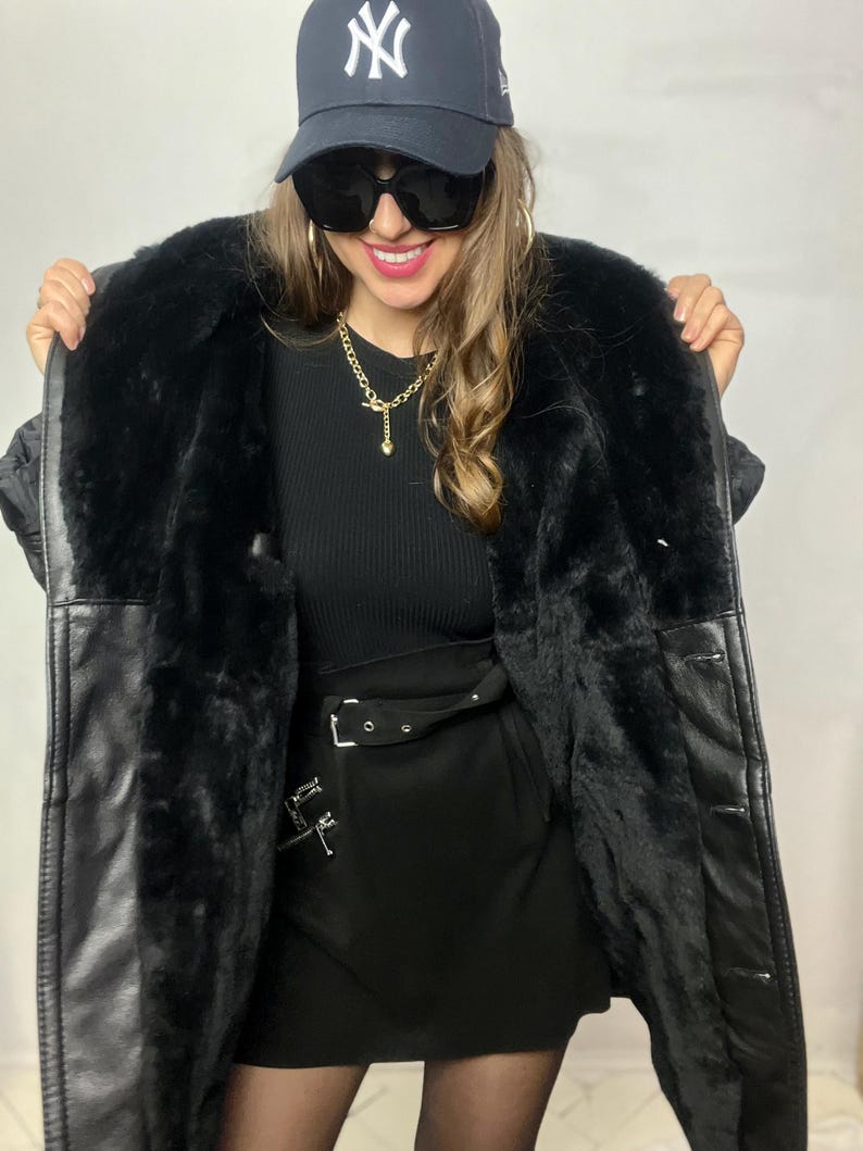 May include: A black faux fur lined leather jacket with a black mini skirt and a black baseball cap with a white "NY" logo.