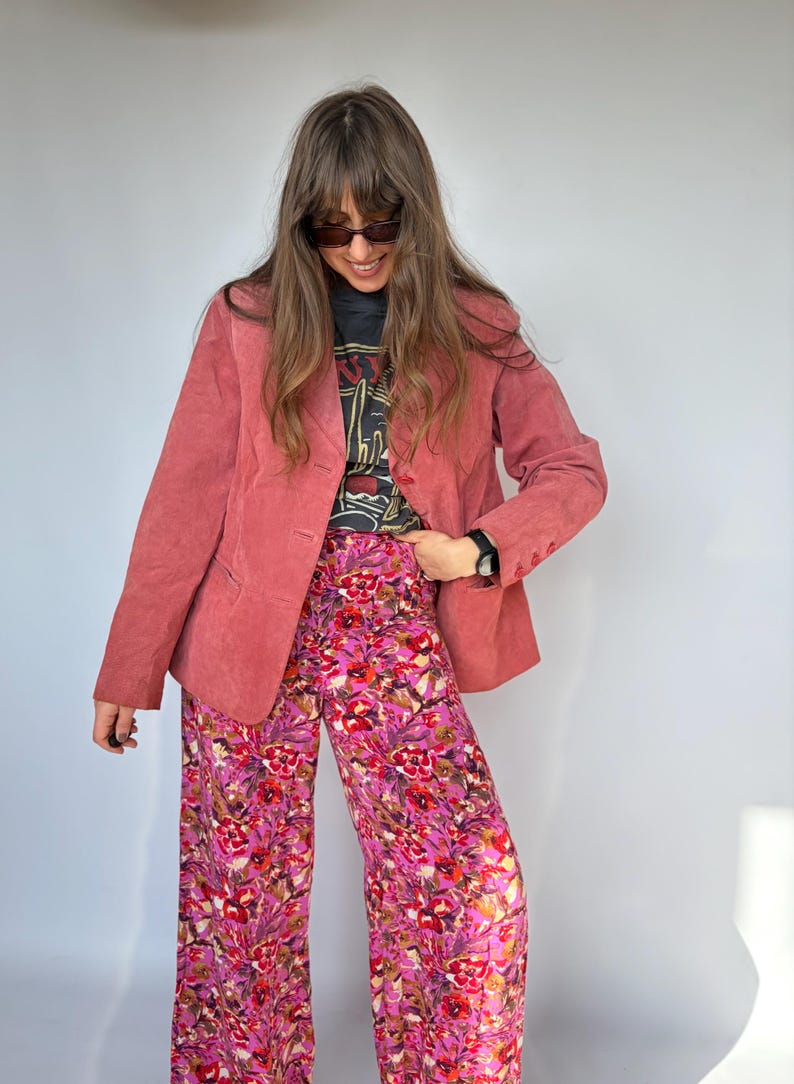 May include: A dusty rose blazer with a three-button closure is paired with wide-leg floral pants in shades of pink and purple. The outfit includes a black graphic tee. The ensemble is a stylish, vintage-inspired look.