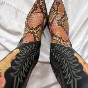 Puede incluir: Botas de vaquero con estampado de piel de serpiente en la punta y la ca&ntilde;a. Las botas tienen una base de cuero negro con costuras decorativas en color verde claro.
