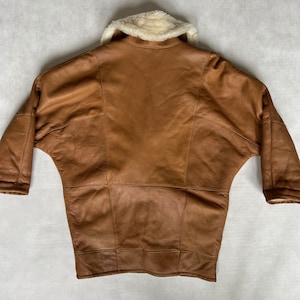 May include: A brown leather jacket with a white faux fur collar. The jacket has a long, loose fit and is made of a soft, supple leather.