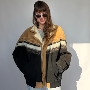 Könnte beinhalten: Vintage Jacke mit einem Farbblock-Design in Beige, Schwarz und Creme. Sie hat einen Shearling-Kragen und eine Knopfleiste. Die Ärmel sind dunkelbraun. Die Jacke wird mit hellblauen Jeans getragen.