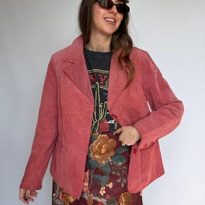 May include: A dusty rose blazer with a three-button closure and notched lapels. The blazer is paired with a floral print skirt and a black graphic tee. The tee features a cactus design and the text "NY".