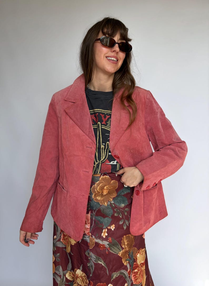 May include: A dusty rose blazer with a three-button closure and notched lapels. The blazer is paired with a floral print skirt and a black graphic tee. The tee features a cactus design and the text "NY".