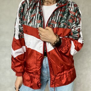 May include: A red, white, and green patterned jacket with a zipper closure. The jacket has a white stripe down the sleeves and a white stripe across the chest. The jacket is made of a shiny material.
