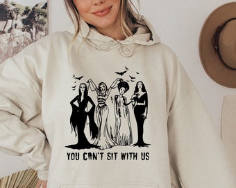 May include: A cream-colored hoodie with a black graphic of four women in long dresses and the text "You can't sit with us".