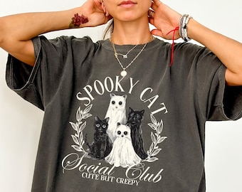 May include: A dark gray oversized t-shirt with a graphic print of three cats, two white and one black, with the text "Spooky Cat Social Club Cute But Creepy".