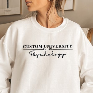 May include: White sweatshirt with black text that reads "CUSTOM UNIVERSITY Est. 1971 Psychology".