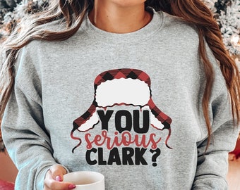 Può includere: Felpa grigia con la scritta "YOU serious CLARK?" in rosso e nero, con un design a cappello a scacchi. Questo capo festivo fa parte di una collezione di abbigliamento a tema natalizio.