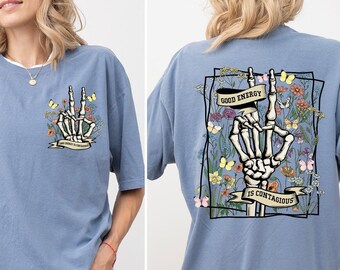 May include: A blue jean oversized t-shirt with a skeleton hand graphic and the text "Good energy is contagious" surrounded by flowers and butterflies.