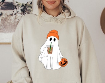 May include: A beige hoodie with a graphic of a ghost wearing an orange beanie and holding a pumpkin and a cup of coffee.