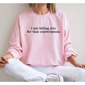 May include: A pink sweatshirt with the text "I am billing you for this conversation." printed on the front.