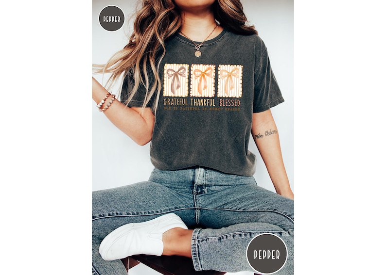 May include: Dark gray t-shirt with the words "Grateful Thankful Blessed" and three bow designs. The shirt is worn with blue jeans and white shoes. The overall theme is gratitude and blessings.