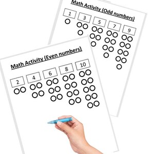 Può includere: Due fogli bianchi con attività di matematica per numeri pari e dispari. I fogli hanno numeri e cerchi per contare. Una mano tiene una matita blu, pronta a completare l'attività.