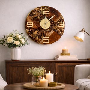 May include: A circular wall clock with gold numerals and hands, featuring a brown and tan textured face. The clock is mounted on a light-coloured wall above a dark wood cabinet. A bouquet of white flowers sits in a white vase.