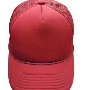 May include: A burgundy trucker hat with a mesh back and a curved brim. The front panel is solid burgundy, and the brim has a stitched design. The hat has a classic, casual style.