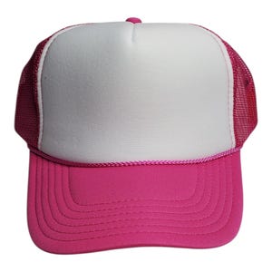 May include: A pink trucker hat with a white front panel and a pink brim. The hat features a pink mesh back and a pink rope detail along the brim. The hat has a curved brim and a pink button on top.