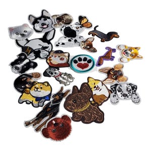 May include: A selection of embroidered patches depicting different dog and cat breeds. The patches display detailed designs, including a husky, dachshund, dalmatian, and a cat with a hat. The patches are in various colours and sizes, with a paw print patch in the centre.