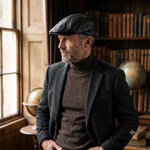 May include: A black leather flat cap featuring a quilted geometric pattern across the crown and a small adjustable side strap with a metal buckle. The cap has a structured brim and a smooth finish, designed with a classic silhouette and stitching.