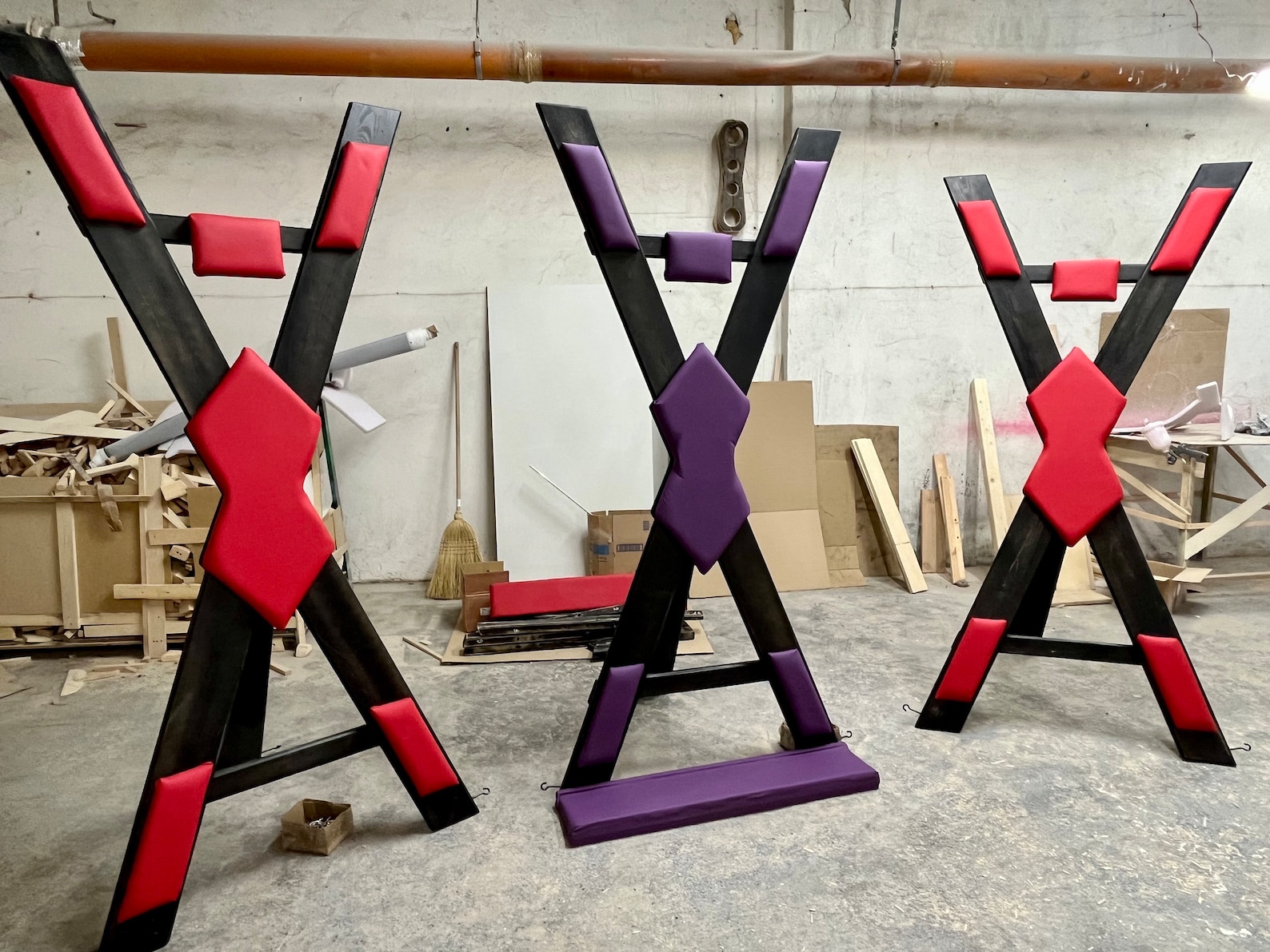 Custom St. Andrew’s Crosses in red and purple—versatile BDSM furniture for bondage rooms and sex dungeon ideas.