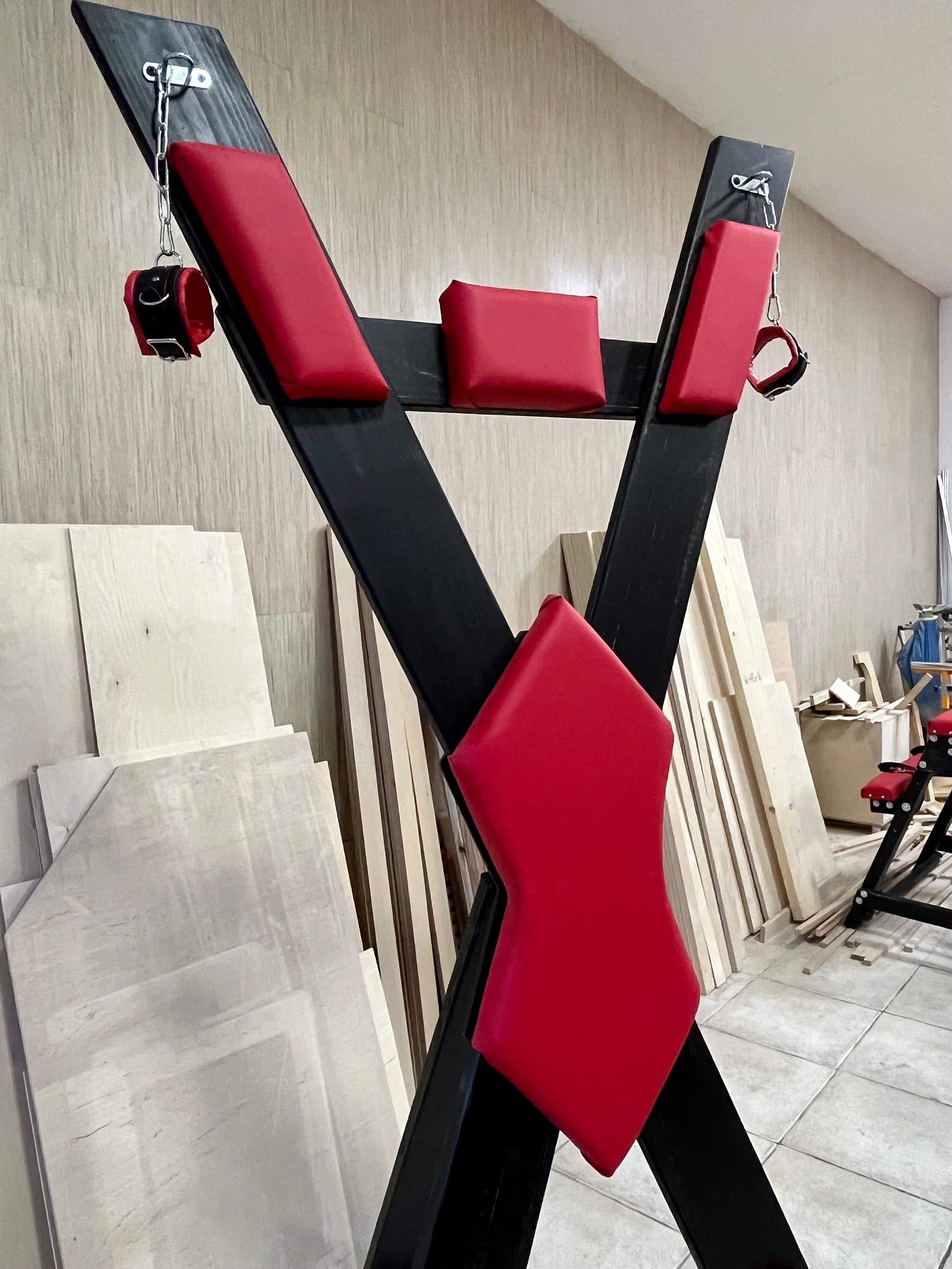 Close-up of BDSM St. Andrew’s Cross with red restraints and padding—bondage furniture for sex dungeon or playroom use.
