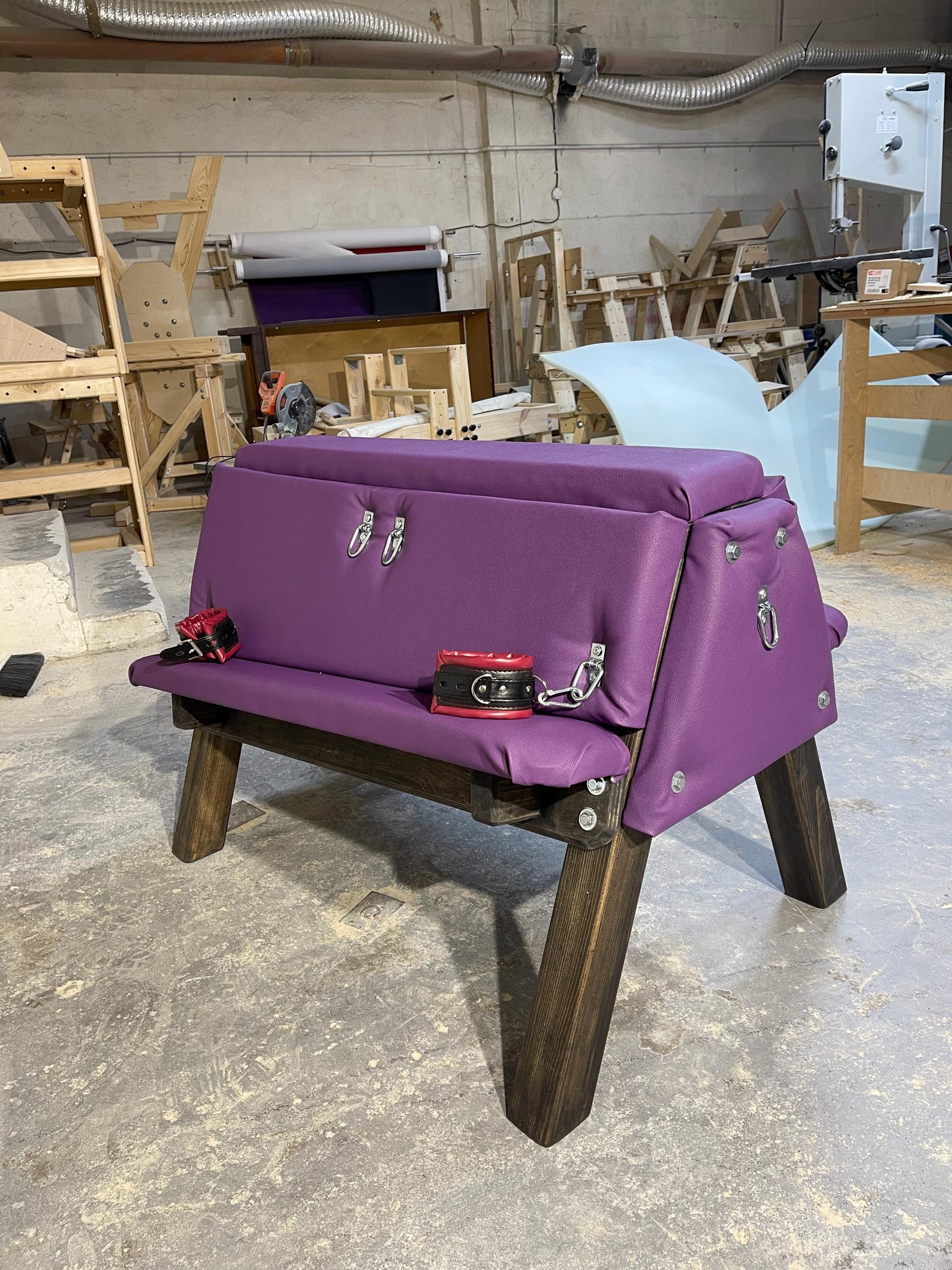 Purple padded bdsm bench with wood frame and red restraints, designed for sex dungeon or bondage room furniture setups.
