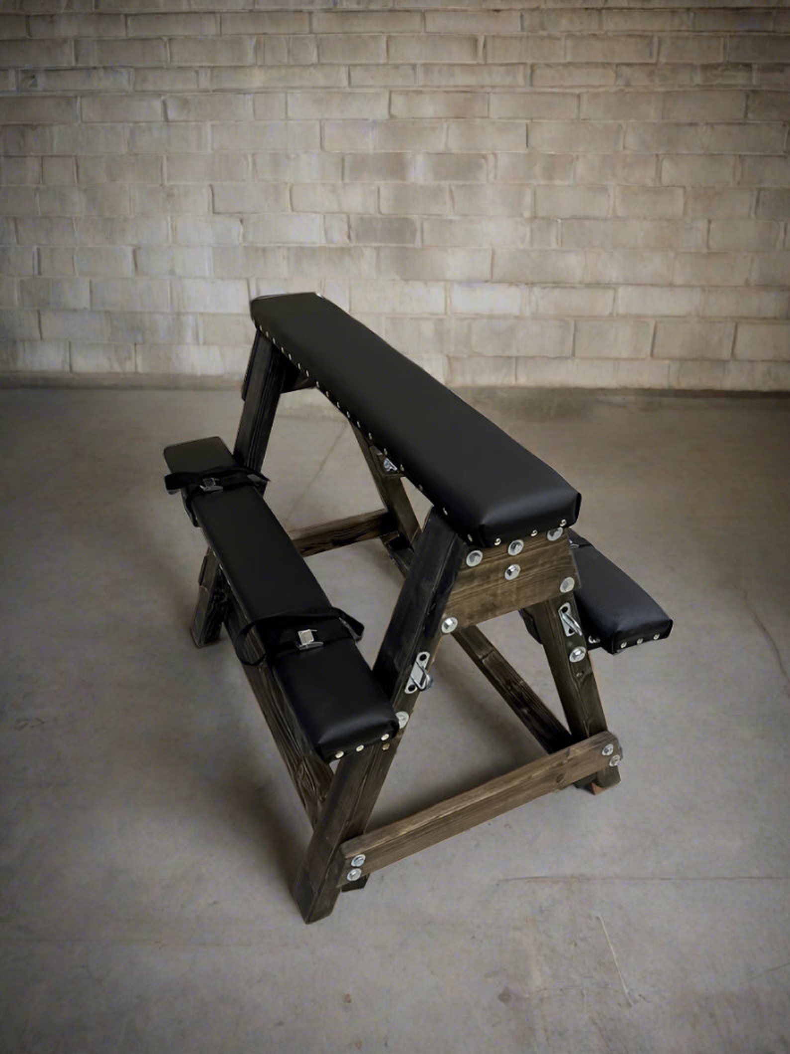 Dark wood bdsm bench with black padded restraints, designed as durable bondage furniture for a discreet sex dungeon setup.