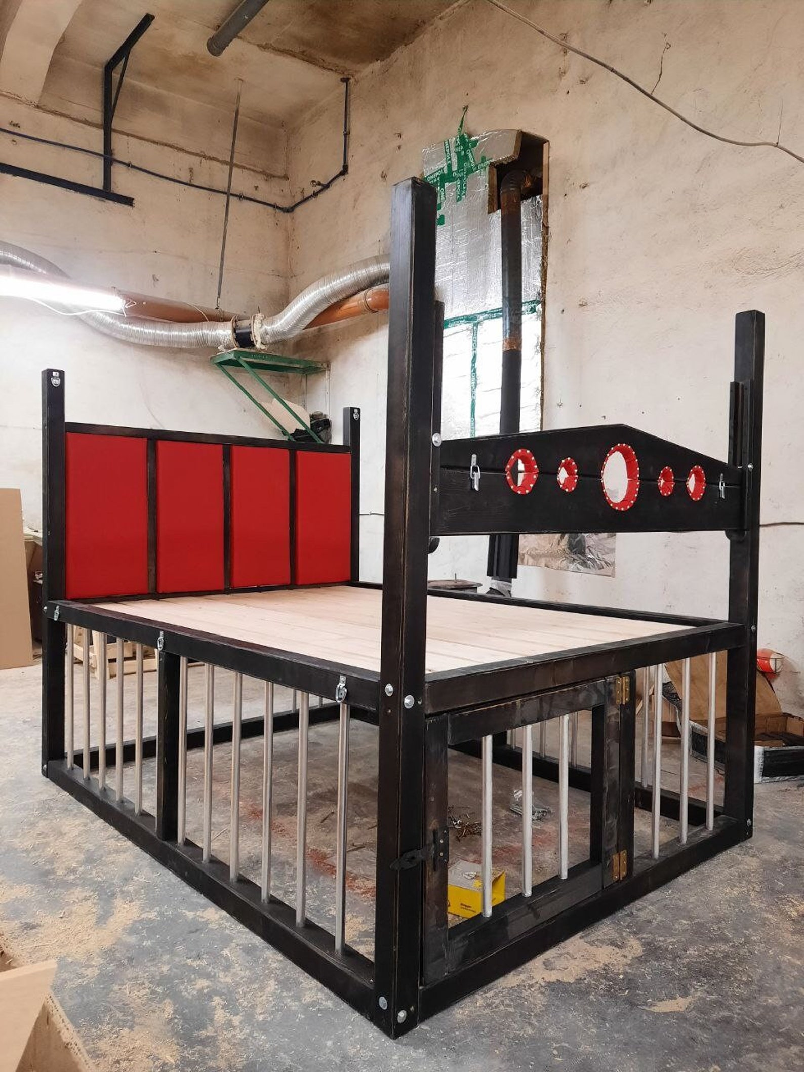 Handcrafted king size bondage bed with under-bed cage, red padded headboard, and bondage restraints for bdsm room setups.