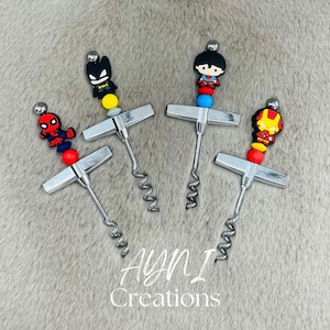 Könnte beinhalten: Vier silberne Weinöffner mit Superhelden-Figuren. Jeder Öffner zeigt einen anderen Charakter: Deadpool, Batman, Superman und Iron Man. Die Öffner haben einen silbernen Korkenzieher und einen Griff mit bunten Perlen.