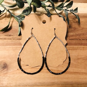 May include: A pair of teardrop-shaped earrings with black and silver beads. The earrings are silver at the top and black at the bottom.