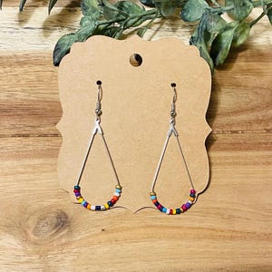 May include: A pair of dangle earrings with a teardrop shape. The earrings are made of silver wire and have colorful beads strung along the bottom.