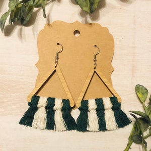 May include: A pair of green and white tassel earrings with wooden triangle shapes. The earrings are hanging from a brown card.