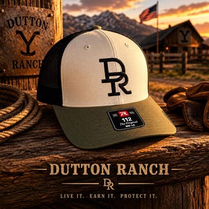 May include: A baseball cap with a cream-colored front panel featuring a black DR logo, a black mesh back, and an olive green brim. A black sticker on the brim displays the text 112 The Original MD-LG. The cap is positioned on a wooden surface.