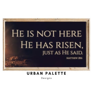 May include: A framed print with a dark background and a quote in white text: "He is not here. He has risen, just as he said. Matthew 28:6". The print has a wooden frame and the words "Urban Palette Designs" are printed below the frame.