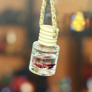 May include: A clear glass bottle with a white lid and a string hanging from it. The bottle contains a clear liquid and a few dried rose petals.