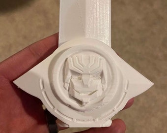 Puede incluir: Modelo de cabeza de robot de plástico blanco impreso en 3D con un diseño detallado. La cabeza del robot está rodeada por un anillo circular con una superficie texturizada.