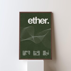 May include: A framed art print with the word "ether" in white, above a white, wavy line design on a dark green background. The print includes text describing the ether as the unseen fabric of existence.