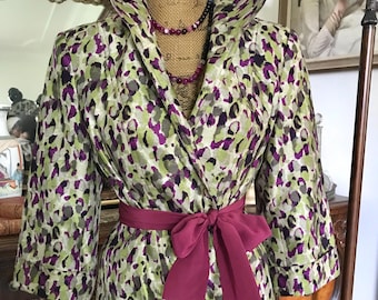 May include: A patterned wrap jacket with a wide collar and three-quarter sleeves. The jacket features a print in shades of green, purple, and grey. A burgundy sash is tied at the waist. A beaded necklace is visible at the neckline. The jacket is displayed on a mannequin.