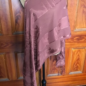 Könnte beinhalten: Ein mauvefarbener Schal mit Paisley-Muster und Fransen. Der Schal ist über eine Schaufensterpuppe gelegt und hat eine silberne Halskette um den Hals.