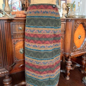 May include: A long, wrap-style skirt with a colourful geometric pattern. The skirt features horizontal stripes in shades of red, green, blue, and tan. It is fastened with a single button. The skirt is displayed on a mannequin.
