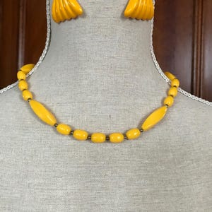 May include: A vintage jewelry set featuring a necklace and matching clip-on earrings. The necklace has yellow beads with a mix of shapes, and the earrings are a fan-like design. The set is displayed on a mannequin.