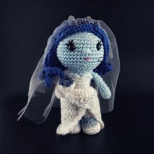 May include: A crocheted doll wearing a white dress and a blue veil. The doll has blue hair, blue eyes, and a pink mouth.