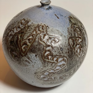 Puede incluir: Un jarrón redondo de cerámica azul claro con un esmalte marrón y un diseño de hojas estilizadas.