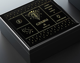May include: Black wooden box with a gold design featuring the zodiac sign Gemini. The box is open and the inside is lined with white felt.