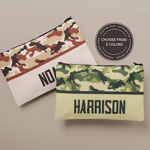 May include: Two personalized camouflage makeup bags. One bag is brown and tan camouflage with the name "Nolan" on it. The other bag is green and tan camouflage with the name "Harrison" on it.  The bags are both made of canvas and have a zipper closure.
