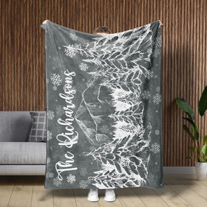 May include: A gray fleece blanket with a white design of a mountain range and trees. The text "The Richardsons" is written in white on the blanket.