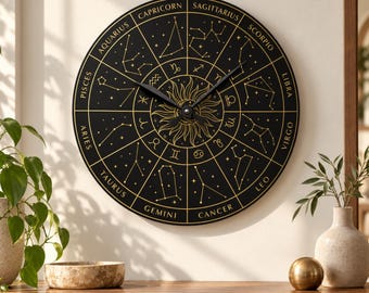 Puede incluir: Un reloj de pared circular con esfera negra que presenta signos del zodiaco, constelaciones y los nombres de los doce signos en color dorado alrededor del borde. Una ilustración de sol estilizada se sitúa tras las manecillas negras.